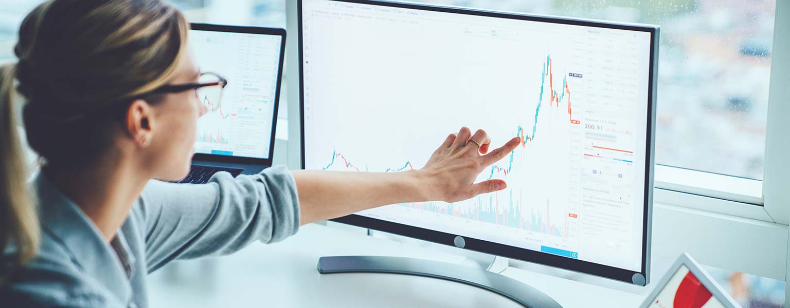 young woman pointing at monitor with sales graph on it